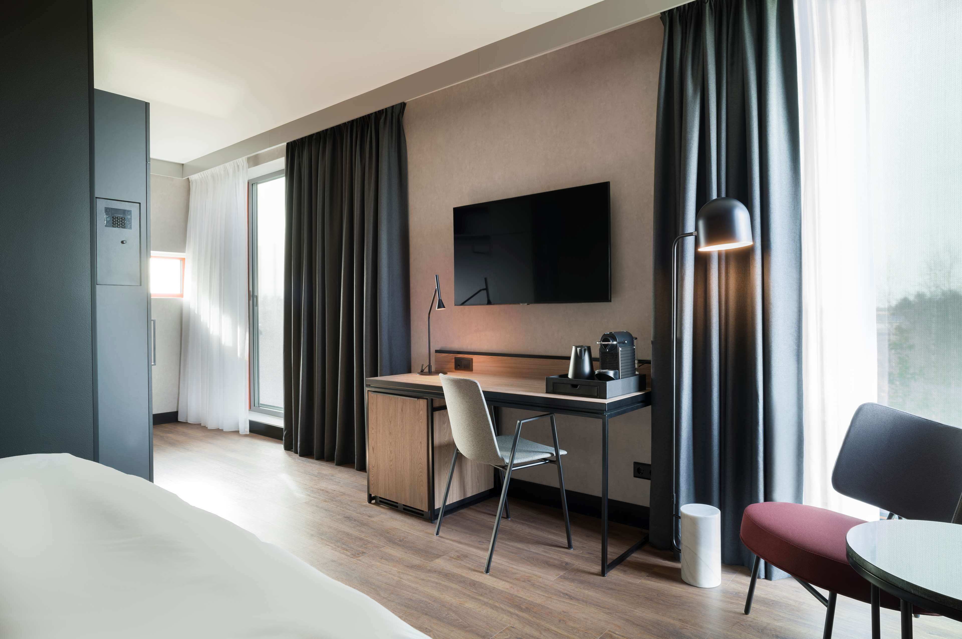 Una habitación de hotel moderna con una cama, un escritorio con una silla, un televisor y una lámpara.