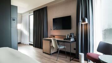 Una habitación de hotel moderna con una cama, un escritorio con una silla, un televisor y una lámpara.