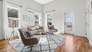Un salón amplio con sofá, sillón y mesa de centro, ventanas grandes y vistas al exterior.