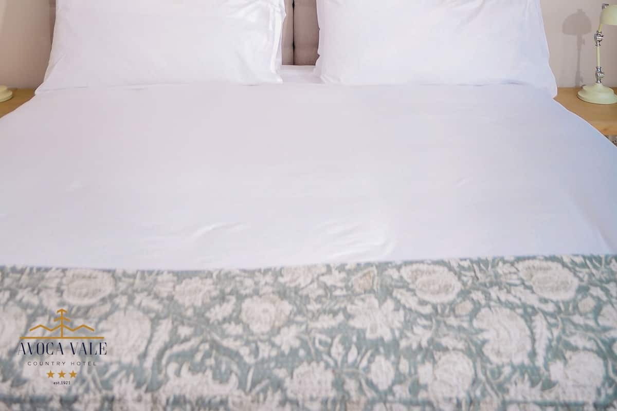 Quarto de hotel com cabeceira estofada, cama com roupa de cama branca e unidade de ar condicionado fixada na parede.