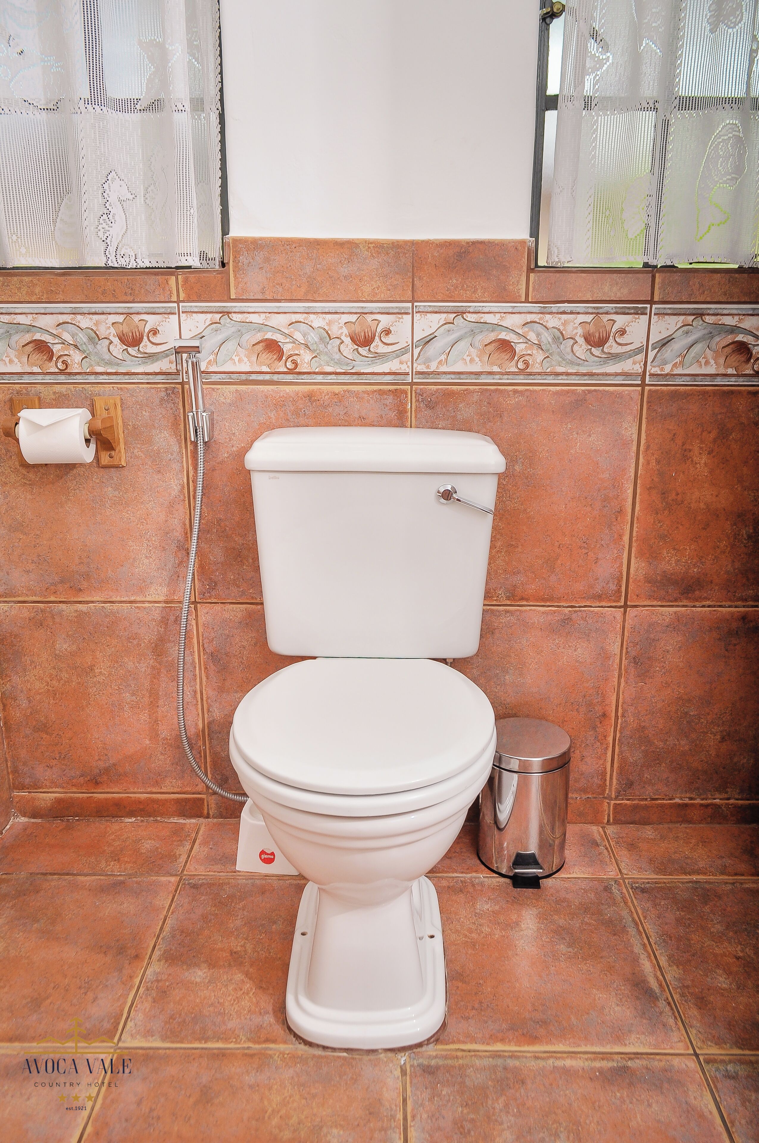 Un baño con inodoro, cubo de basura y dispensador de papel higiénico.