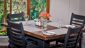 Una mesa de comedor dispuesta con cuatro sillas, un jarrón con flores, saleros y pimenteros, y un mantel individual.