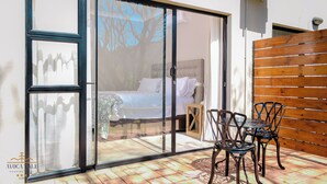 Un dormitorio con cama, pared de madera y puerta de cristal que da a un patio con mesa y sillas.