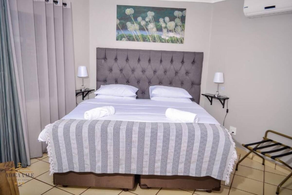 Cama bem arrumada com manta listrada, duas luminárias de cabeceira e ar-condicionado fixado na parede.