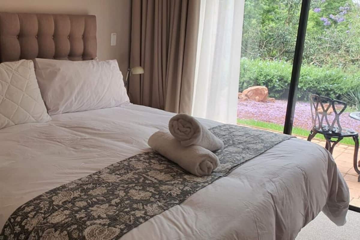 Uma cama grande com cabeceira estofada, colcha estampada e toalhas dobradas sobre a cama.