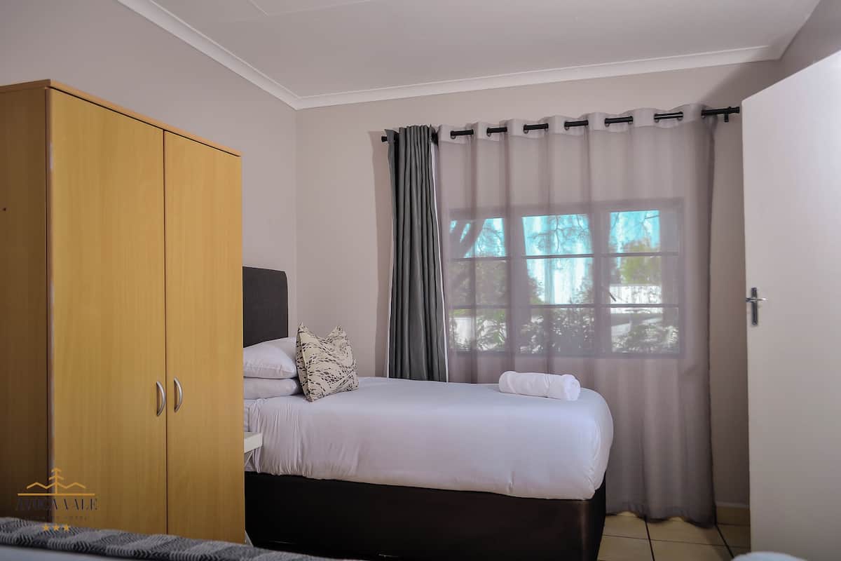 Um quarto com cama, guarda-roupa e janela com cortinas.