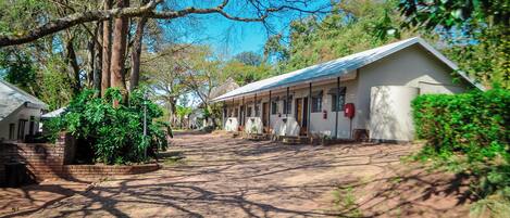 Hotel campestre com um pátio pavimentado, rodeado por árvores e edifícios com arquitetura simples.