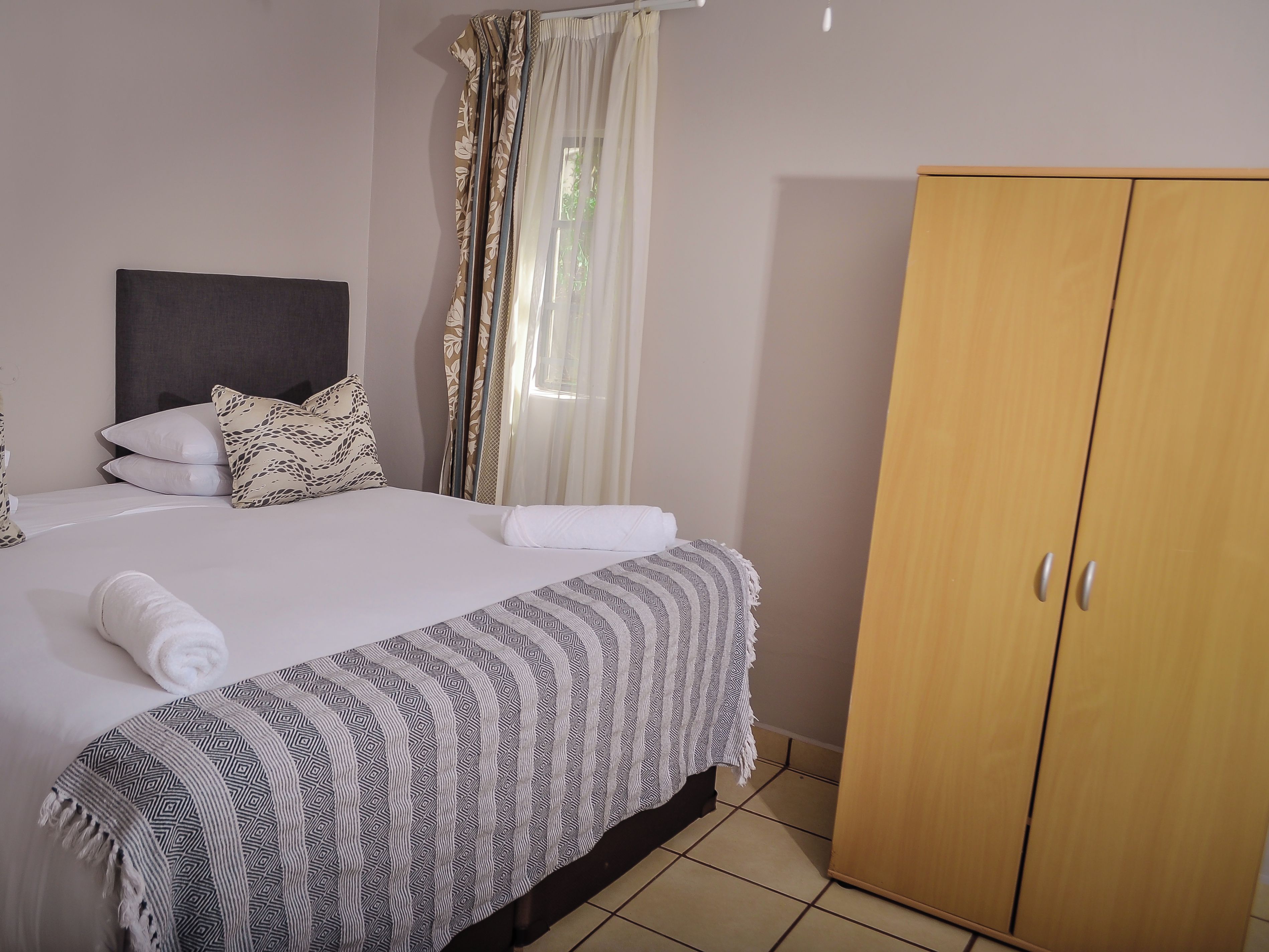 A hotel room with a bed, a wardrobe, and a window with curtains.