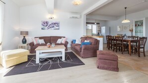 A spacious living room with a sofa, ottoman, and coffee table, a dining area with chairs and a table, and a kitchen in the background. - Villa with pool, 6 persons, large garden with barbecue. Dogs are welcome! (Sv. Lovrec)