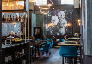 Zona de bar com diversos tipos de garrafas, uma cesta de frutas e área de estar com cadeiras e mesas azuis.