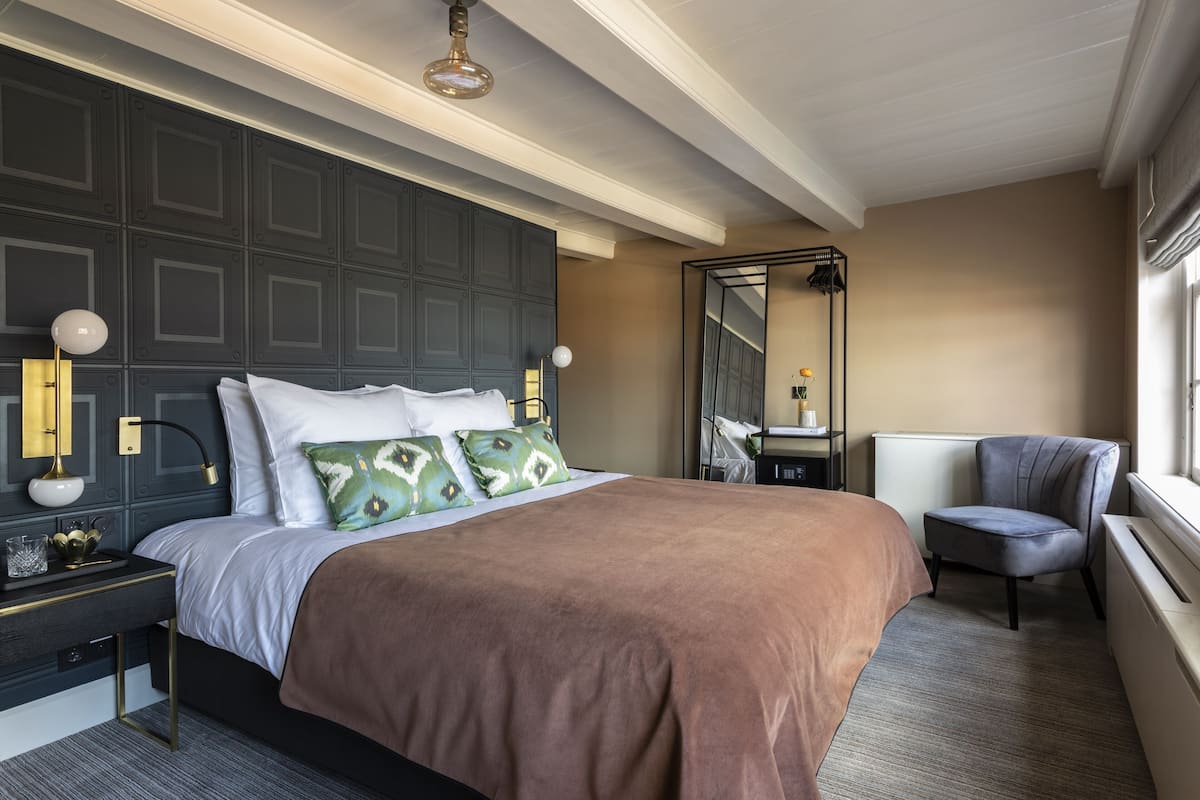 Una habitación de hotel con una cama grande, una mesita de noche, una silla, un espejo y una ventana.
