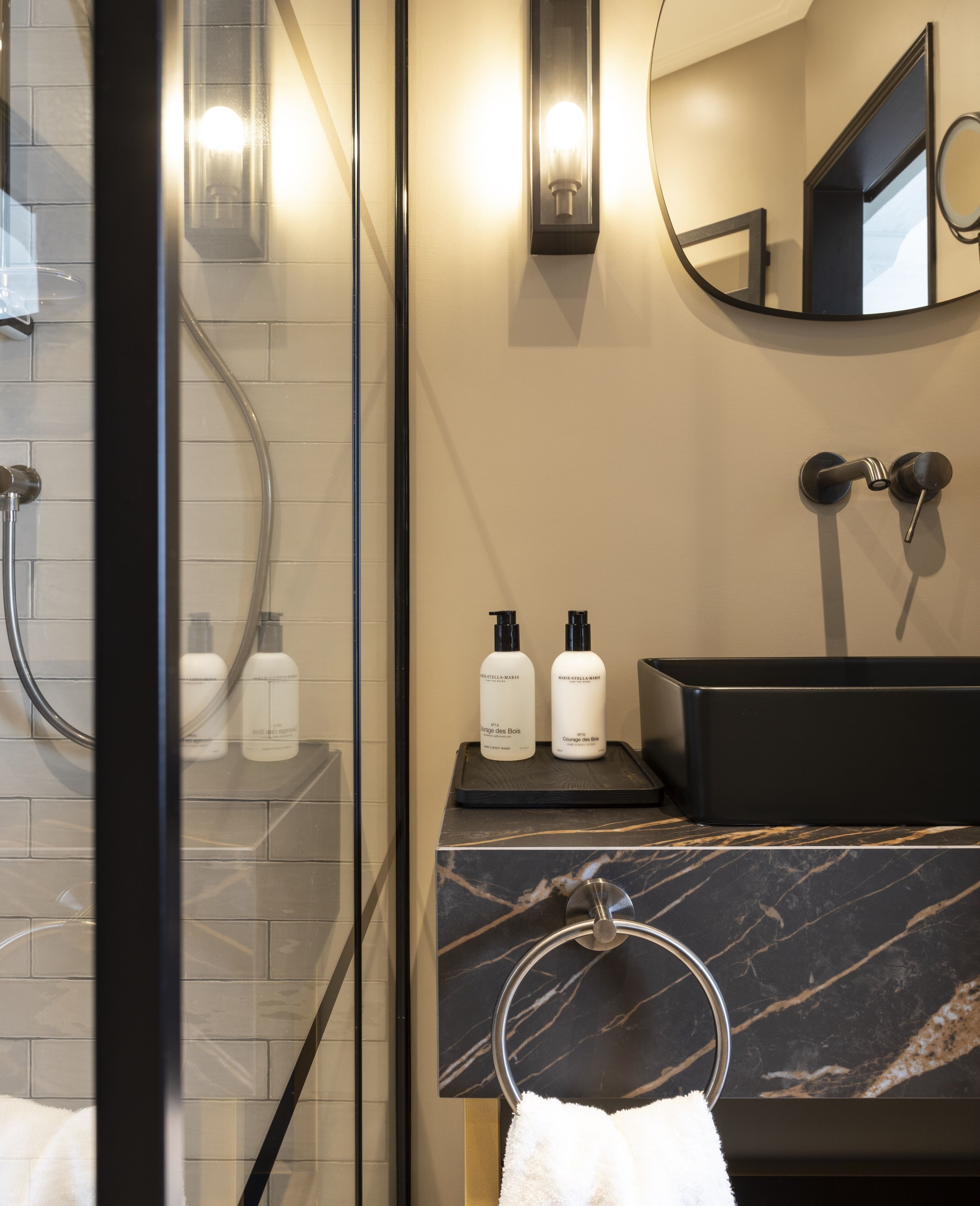 Une salle de bain moderne avec une douche à parois de verre, un lavabo en marbre et deux bouteilles de shampoing posées sur le comptoir.