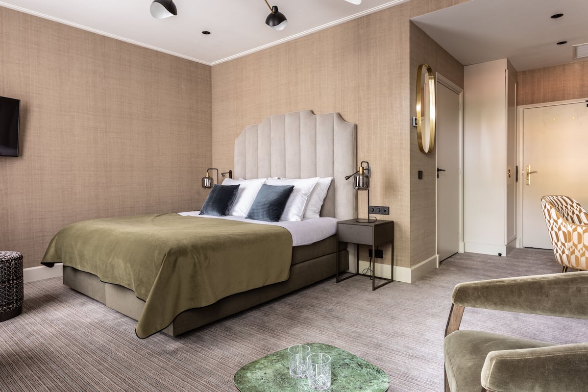 Una habitación de hotel moderna con una cama grande, lámparas de noche, un televisor de pantalla plana y un otoman verde.