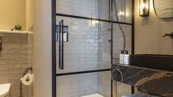 Un baño moderno con ducha de vidrio, lavamanos de mármol y espejo integrado.