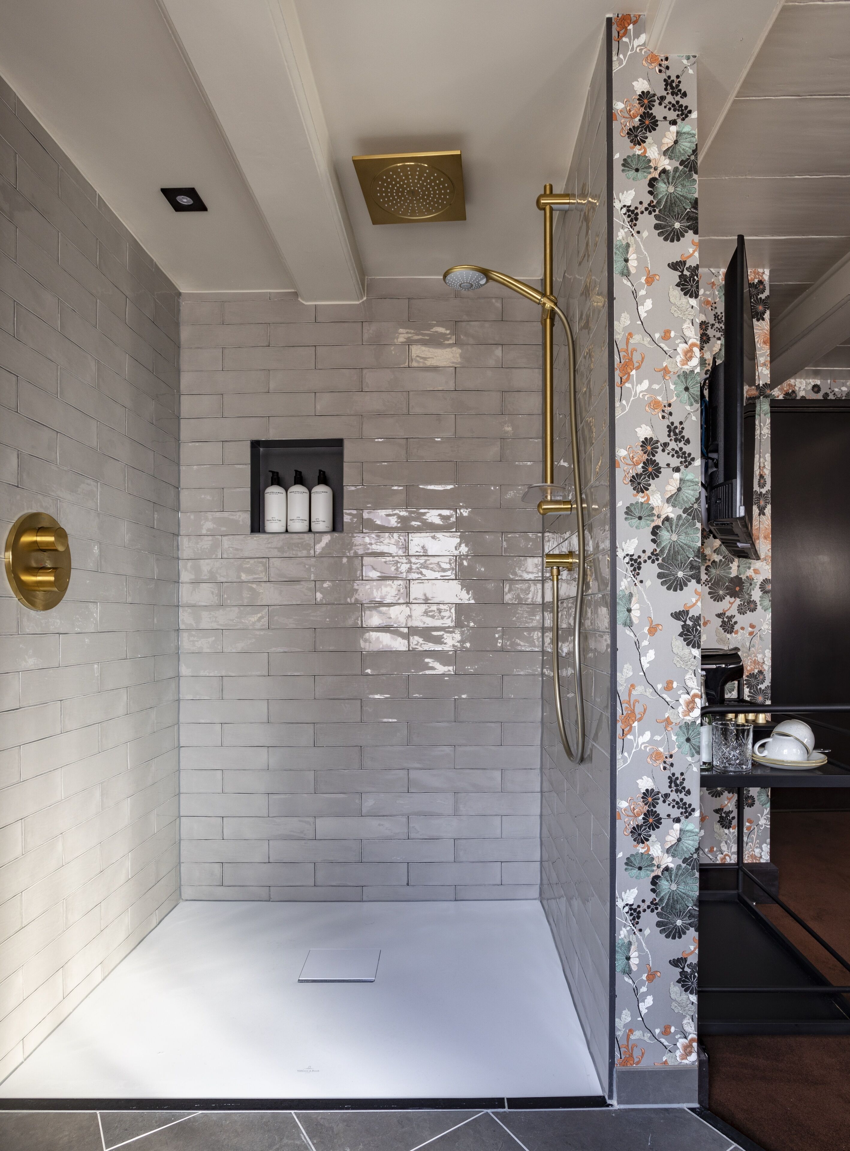 A modern shower room with a tiled floor, a handheld showerhead, and a wall-mounted control panel.