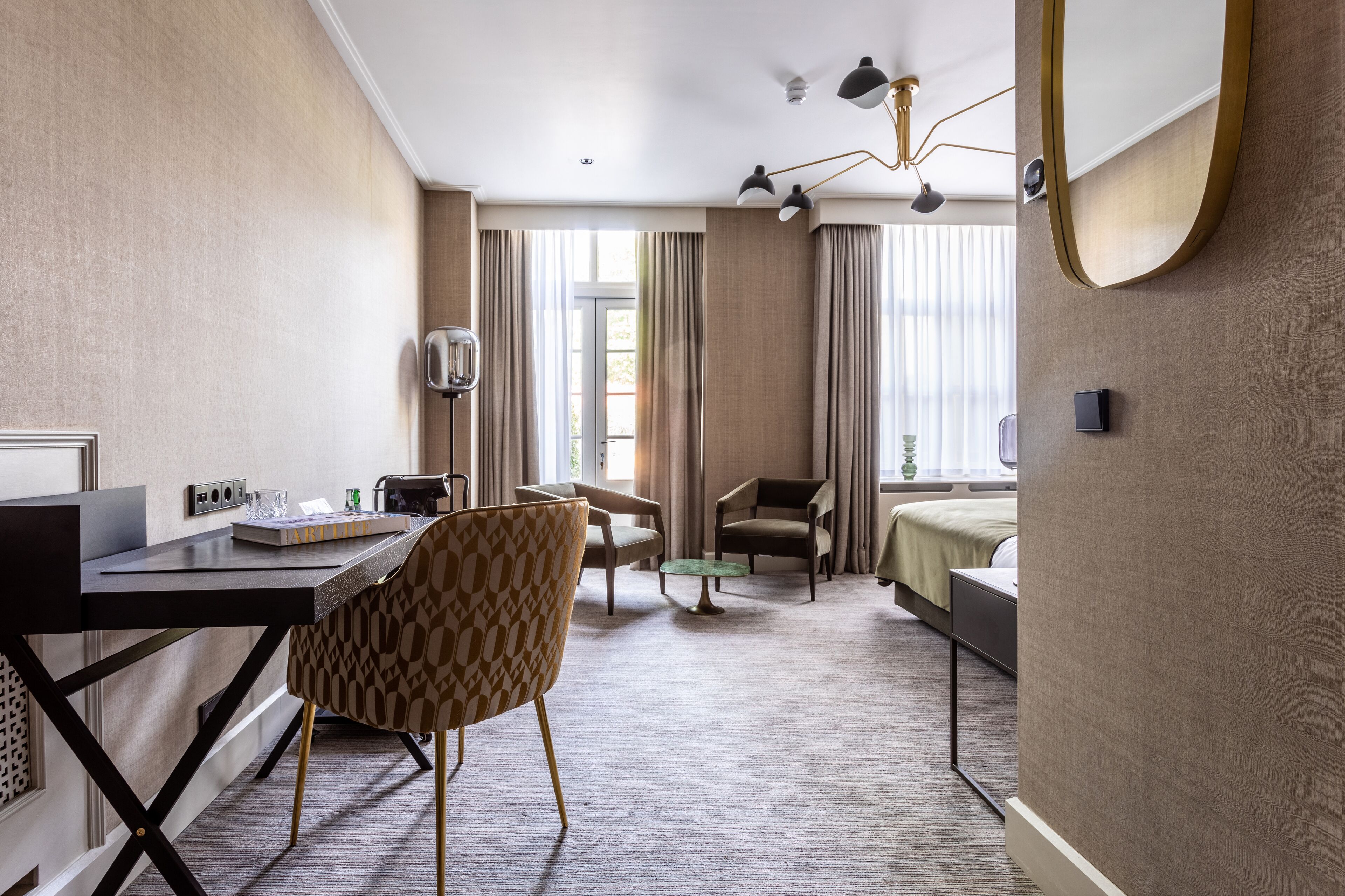 Una habitación de hotel con escritorio, dos sillas, una cama y un espejo grande.