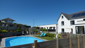 Zona residencial con piscina, jardín cercado y casas con paneles solares.