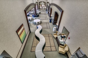 Un amplio vestíbulo de hotel con una zona de estar central curva, varias mesas y un candelabro.