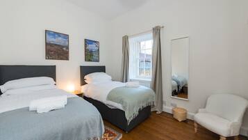 A bedroom with two beds, a window with curtains, a chair, and a mirror.