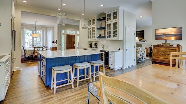 Una cocina amplia con una isla central, taburetes de bar y un comedor con mesa y sillas de madera.