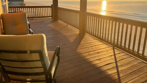 A wooden deck with a chair and a view of the ocean at sunset. - Beachfront, Huge Deck and Private Heated Pool (Bolivar Peninsula)