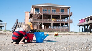 A beach scene with a child playing with a bucket and toy. - Beachfront, Huge Deck and Private Heated Pool (Bolivar Peninsula)