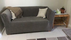 A grey sofa with a brown throw blanket and a beige pillow.