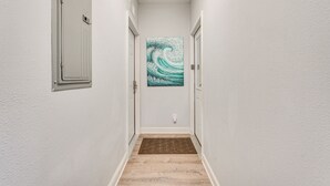 A narrow hallway with white walls, a wooden floor, and a door on the left. - Renovated PCB Studio, 2 Min Walk To Laguna Beach! (Panama City Beach)