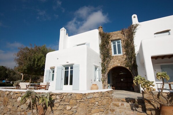 A white building with a stone facade, a wooden door, and a small table with chairs outside.