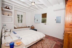 A bedroom with a bed, a bedside table with a plate of food, a window, and a ceiling fan.