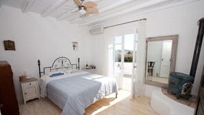 A bedroom with a bed, a nightstand, a dresser, a mirror, and a view of the outdoors. - Architect owned & designed villa (Ano Mera Mykonos)