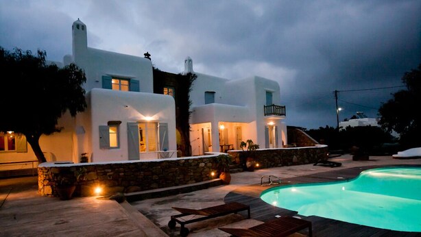 A modern villa with a swimming pool, stone walls, and wooden loungers. - Architect owned & designed villa (Ano Mera Mykonos)