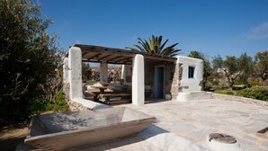 A stone patio with a pergola, a small enclosed structure, and a boat. - Architect owned & designed villa (Ano Mera Mykonos)