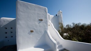 A white, curved architectural feature with a small window and a door, part of a building with a clear blue sky in the background. - Architect owned & designed villa (Ano Mera Mykonos)