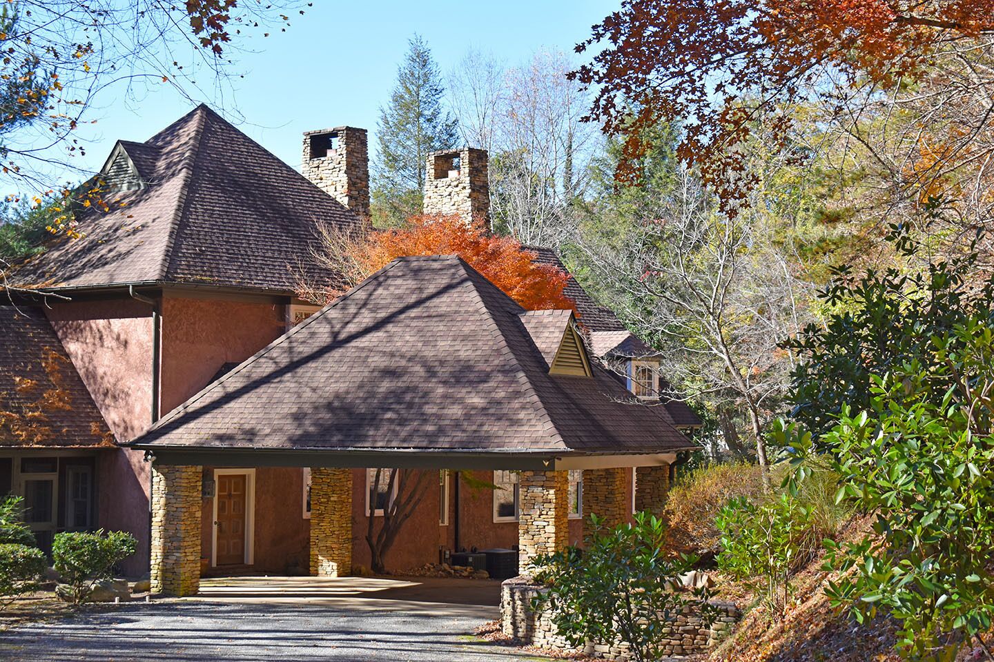 Une maison en pierre avec un toit à forte pente, une cheminée en pierre et un porche à l’avant.