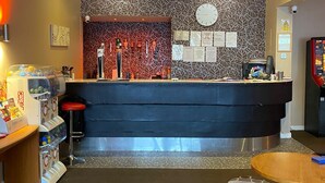 A bar area with a counter, stools, and a ceiling fan. - The Avari Hotel (Blackpool)