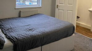 A bedroom with a bed, a window, a radiator, a door, and a bathroom with a sink. - The Avari Hotel (Blackpool)