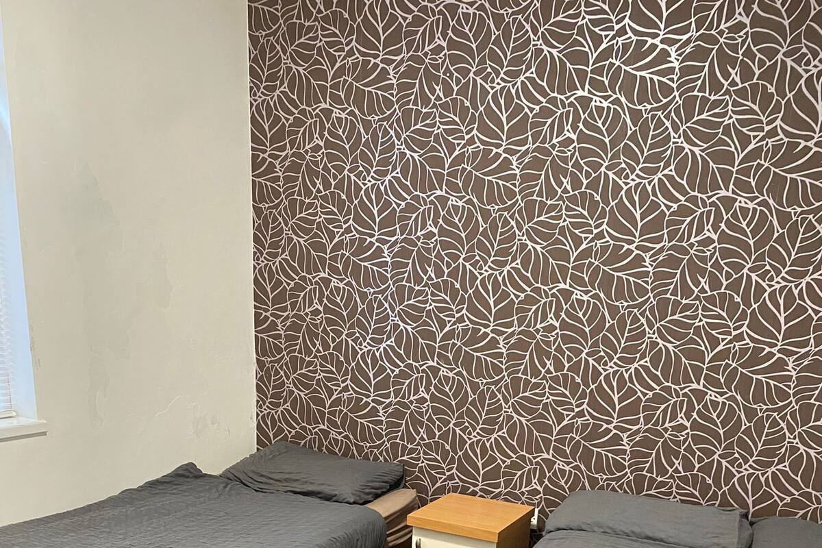 A room with two single beds, a small wooden nightstand, and a patterned wall.
