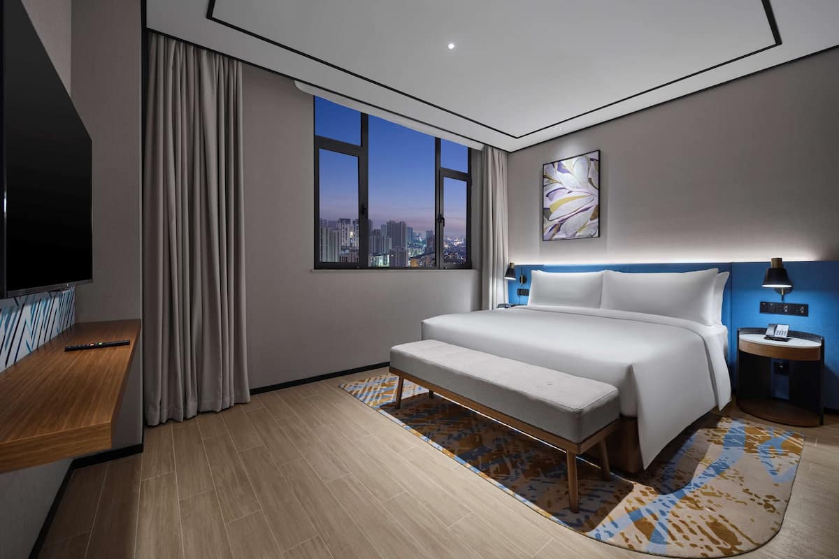 Ein modernes Hotelzimmer mit Blick auf die Stadt, einem großen Bett, einem Schreibtisch und einem Fernseher.