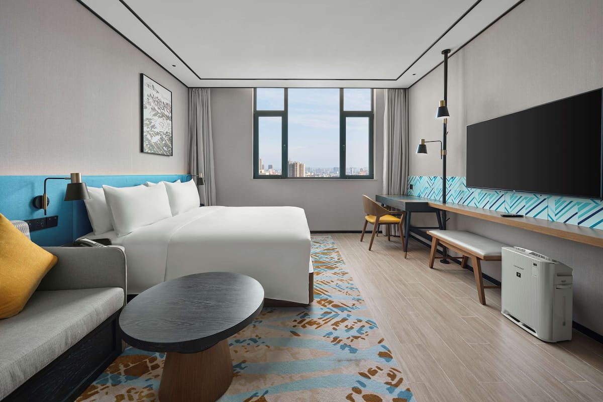 Ein modernes Hotelzimmer mit Bett, einer Couch, einem Schreibtisch und einem Fernseher.