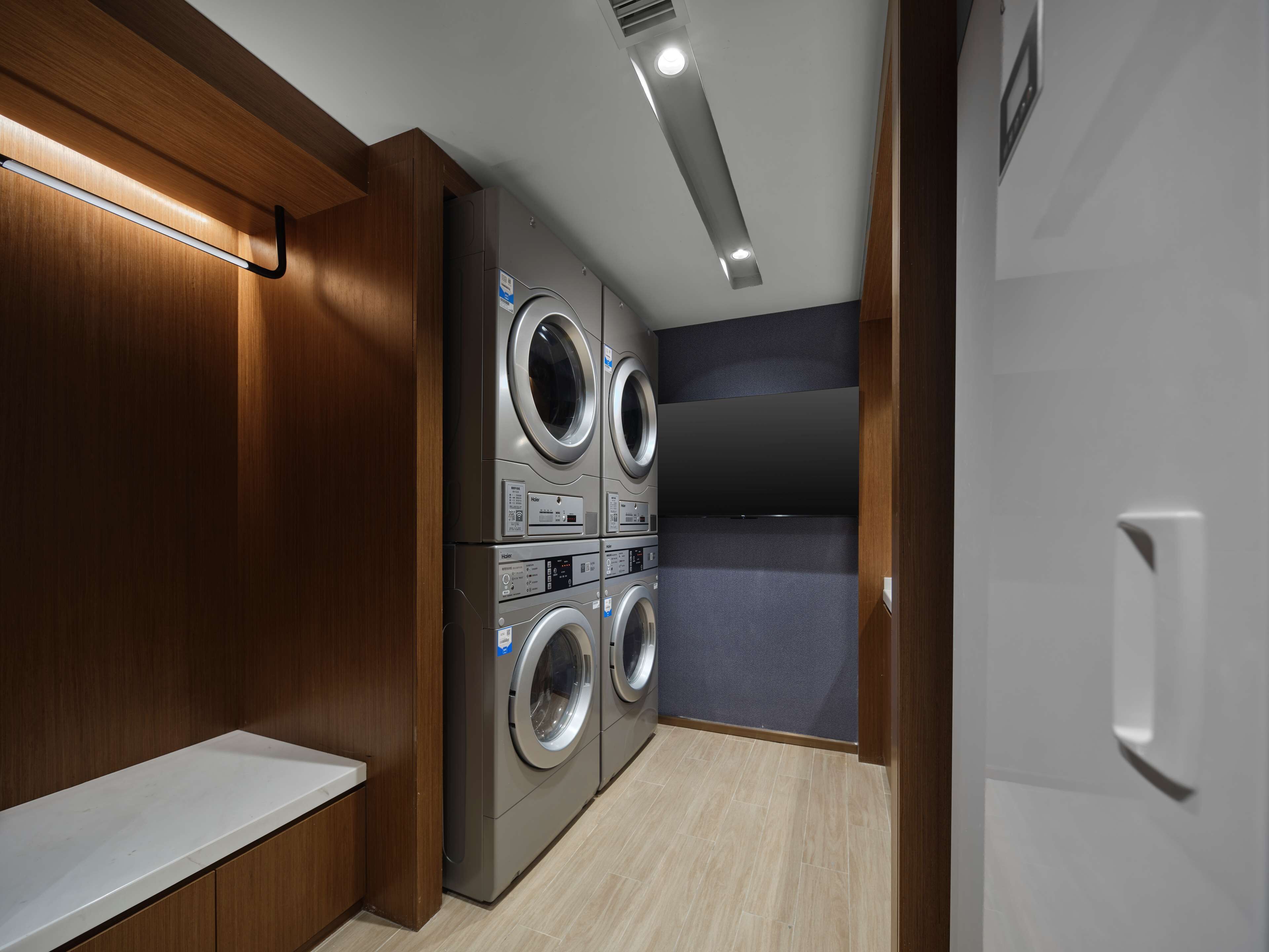 A laundry room with stacked washers and dryers, wooden paneling, and a bench.