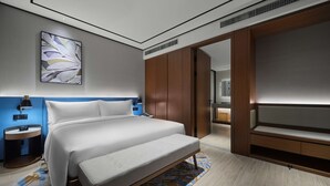 Une chambre d’hôtel moderne avec un grand lit, une table de chevet avec une lampe, une œuvre d’art accrochée au mur et une armoire.