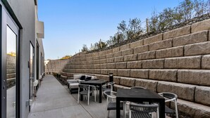 Eine Terrasse mit Sitzgelegenheiten im Freien, eine Steinmauer und ein Gebäude mit großen Fenstern.