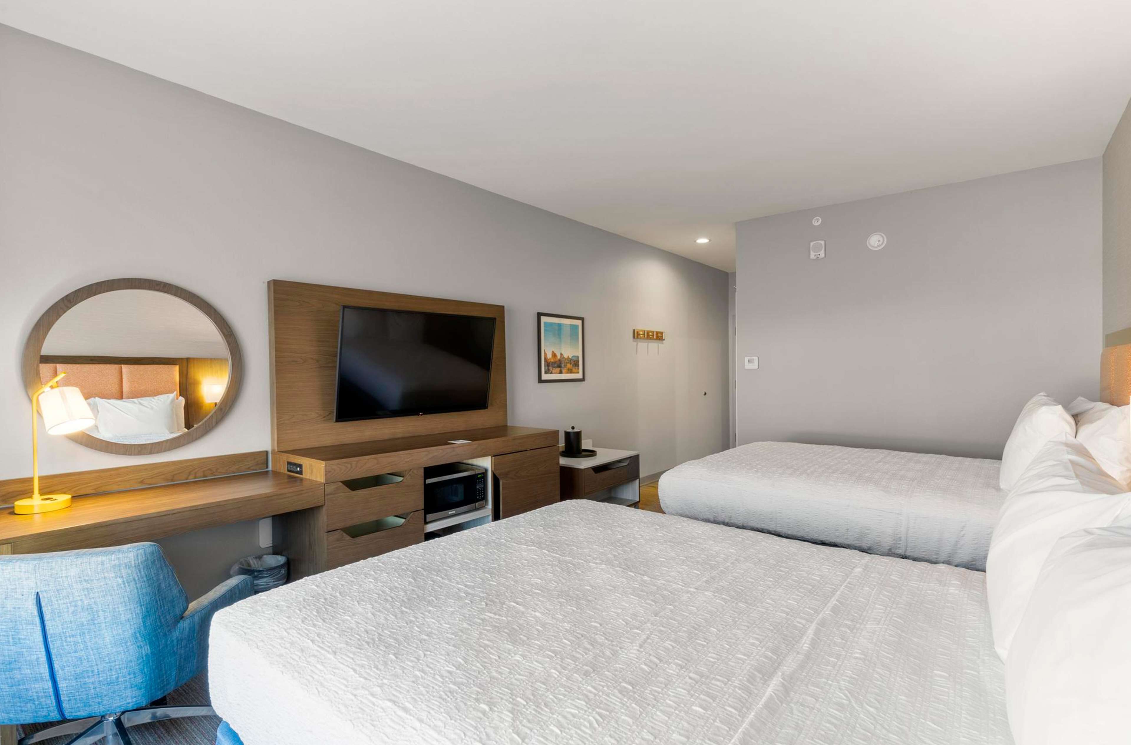 Una habitación de hotel con dos camas, un televisor, un escritorio con lámpara y un espejo.