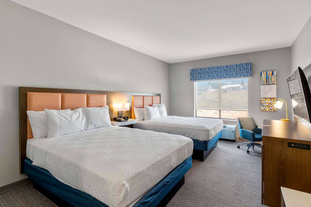 A hotel room with two beds, a desk, and a chair.