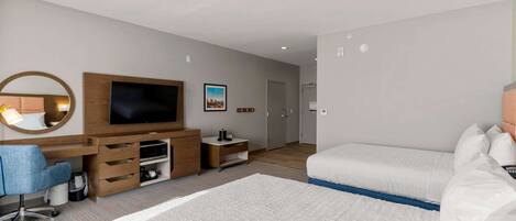 Una habitación de hotel moderna con una cama grande, un escritorio con computadora, una televisión y un pequeño rincón de descanso.