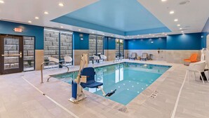 Ein Hallenbad mit blauer und weißer Gestaltung, einem Rettungsschwimmerstuhl und einer Sitzgelegenheit mit Stühlen und Tischen.