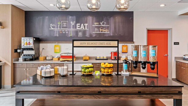 Ein Frühstücksbuffet mit einer Kreidetafel, Kaffeeautomaten und Obstspendern.