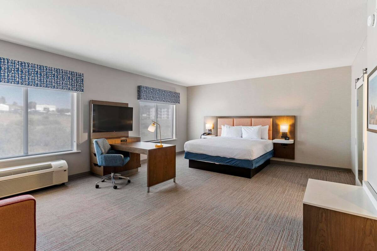 A hotel room with a bed, desk, chair, TV, and a large window.