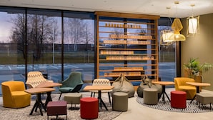 Ein moderner Lounge-Bereich mit bequemen Sitzmöglichkeiten, einem Bücherregal und großen Fenstern mit Blick auf den Parkplatz.
